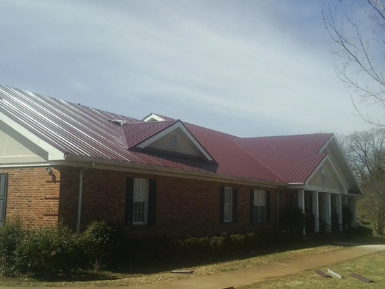 Red metal roof with gabled entries on a long brick building, from a Hail Damage Roof Repair job in Bartlett