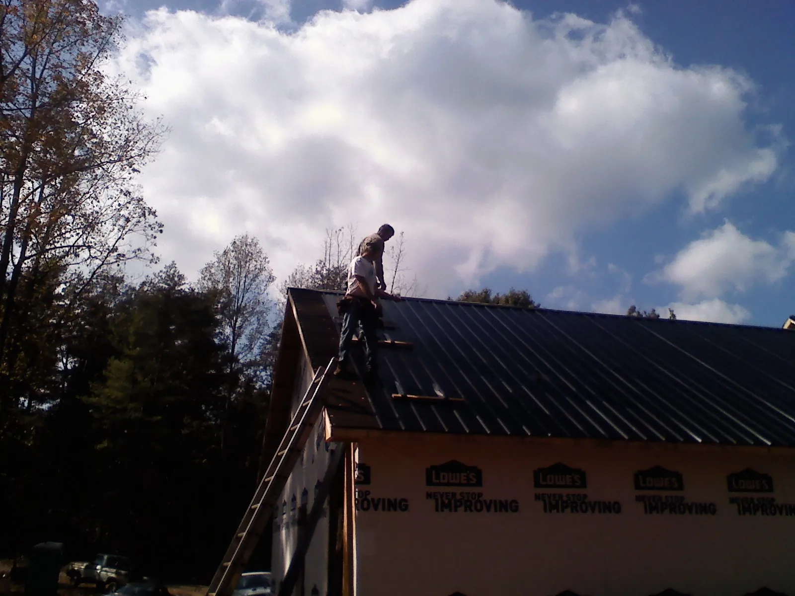Roofer fastening dark metal panels high against a cloudy sky, from a Roof Inspection job in Bartlett
